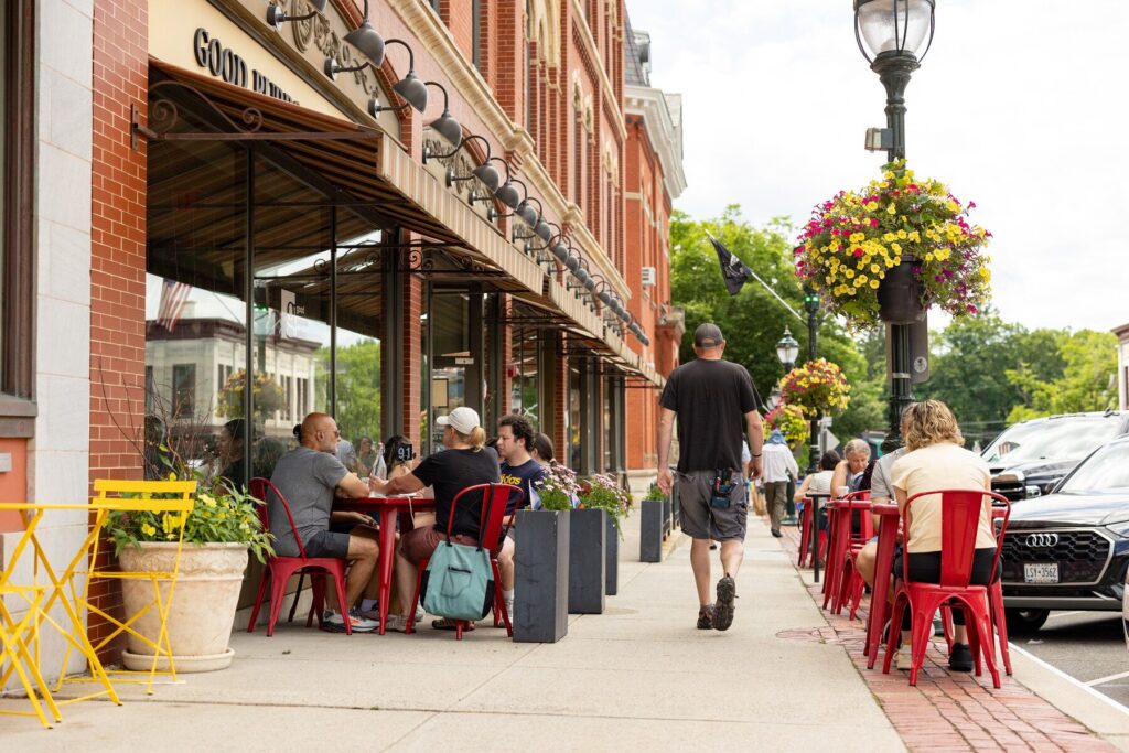 People dining at red cafe tables along Main Street in downtown Lee